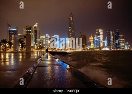 Nächtlicher Blick auf die Skyline von Doha bei Regen in Katar. Silhouette der Frauen auf der Doha Corniche Stockfoto