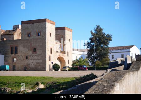 Altes steinerne Festungstor mit Türmen und Nationalflaggen unter einem klaren blauen Himmel in Badajoz, Spanien, zeigt seine reiche Geschichte. Stockfoto