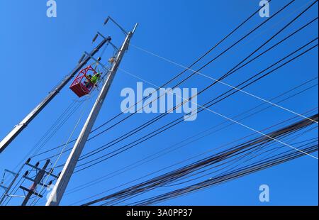 Männer in Arbeitskleidung und Schutzhelmen installieren Hochspannungskabel an einem Strommast. Stockfoto