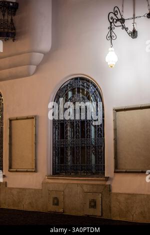 Dekoratives Bogenfenster mit blauem schmiedeeisernem Grill in einem alten Gebäude bei Nacht Stockfoto