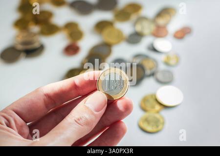 1 Euro-Münze in der Hand vor vielen verschiedenen Münzen im Hintergrund Stockfoto