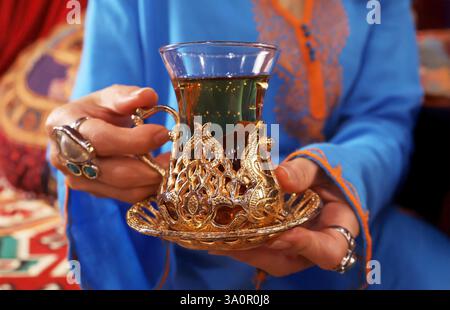 Nahaufnahme einer Hand, die einen heißen türkischen Kräutertee in einem Tulpenglas hält Stockfoto