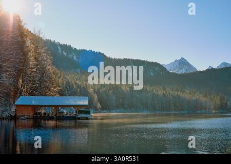 Dieses Foto zeigt eine ruhige Winterszene an einem ruhigen See. Das Bild zeigt ein hölzernes Dock, das in das Wasser hineinreicht und teilweise mit einem s bedeckt ist Stockfoto