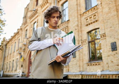 Ein junger Mann in stylischer Freizeitkleidung rezensiert Lehrmaterialien einer alten Ziegeluniversität. Stockfoto