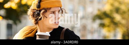 Ein junger Mann schlürft Kaffee im Park, während er die Sonne genießt und Musik hört. Stockfoto