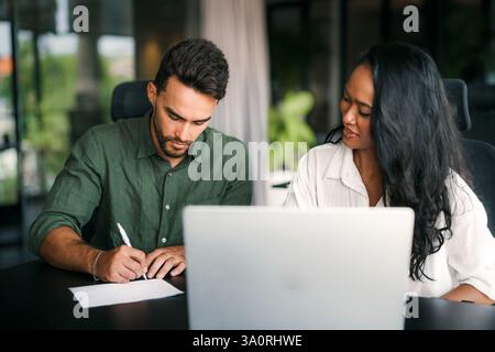 Zwei glückliche, vielseitige Mitarbeiter aus verschiedenen ethnischen Geschäftsbereichen, die im Büro des Unternehmens arbeiten und sich unterhalten Stockfoto