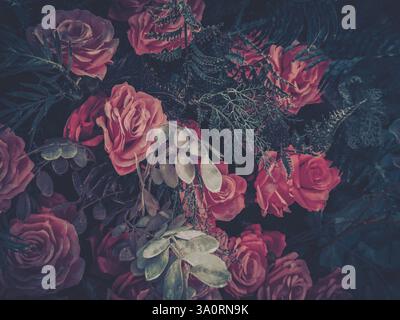 Moody-romantische Arrangements von Kunstblumen. Dunkelrote und rosa Rosen blühen vor einem dunklen, strukturierten Hintergrund. Elegantes florales Stillleben. Stockfoto