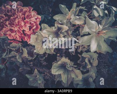Eine Gruppe künstlicher Blumen mit einer großen rosafarbenen Blüte und mehreren weißen Blüten schafft ein etwas dunkles und stimmungsvolles Blumenarrangement. Stockfoto