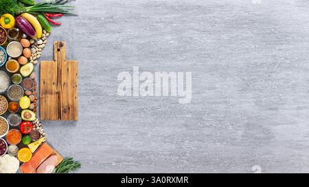 Frische Lebensmittel auf grauem Betonhintergrund mit leerem Schneidebrett, gesunde ausgewogene Ernährung Konzept, Kopierraum, Draufsicht Stockfoto