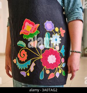 Schwarze Damenschürze mit traditioneller tatarischer Stickerei in Häkeltechnik. Das Blumenmuster enthält leuchtende Blumen und Blätter in Rot und Blau Stockfoto