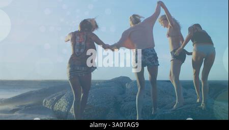 Hände halten und auf Felsen springen, Freunde genießen den Strandtag mit Bokeh-Bild Stockfoto