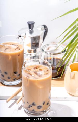 Iced Tapica Coffee Latte oder boba Pearl Bubbles Milchtee, asiatisches trendiges kaltes Kaffeegetränk mit Tapiokasseln und zerstoßenem Eis, auf weißem Marmorhintergrund Stockfoto