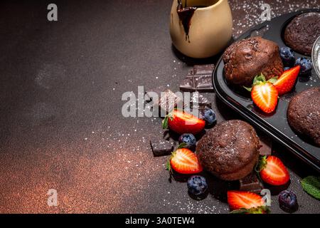 Schokoladen-Muffins mit Beeren. Muffin-Pfanne mit hausgemachten süßen, dunklen Schokoladen-Cupcakes mit Kakaosoße, Zuckerpulver und frischen Erdbeeren, Blaubeeren Stockfoto