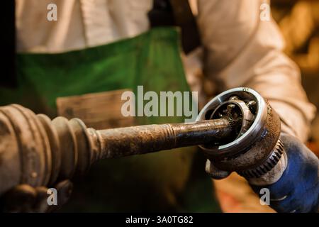 Nahaufnahme eines Mechanikers, der das Antriebswellengelenk eines Fahrzeugs in einer Werkstatt zusammenbaut. Stockfoto