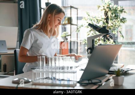 Junge Ärztin im Mantel sitzt in der Klinik und arbeitet. Stockfoto