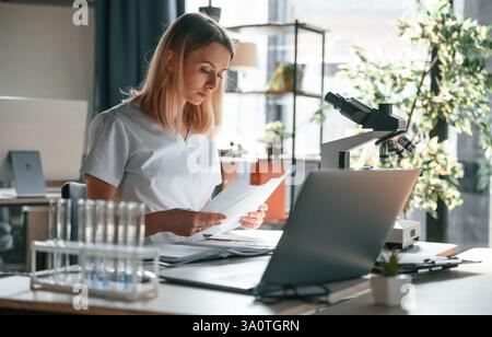 Junge Ärztin im Mantel sitzt in der Klinik und arbeitet. Stockfoto