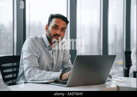 Der schöne indianer arbeitet im Büro mit einem Laptop. Stockfoto