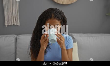 Eine junge Frau genießt einen Kaffee zu Hause im Wohnzimmer mit einem entspannten und ruhigen Gesichtsausdruck Stockfoto