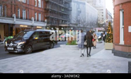Verschwommene Menschen laufen entlang der londoner Straße mit weihnachtsdekorationen, die die urbane Winterszene mit Bokeh-Lichtern und unscharfen Gebäuden darstellen. Stockfoto
