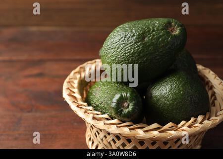 Ganze Avocados in Korb auf Holztisch, Großaufnahme. Leerzeichen für Text Stockfoto