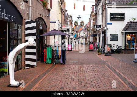 Meppel, Niederlande, 6,9.2024- die Woldstraat in Meppel, Niederlande, mit offenen Boutiquen, hängenden Blumendekorationen über der Straße und einem weißen Stab Stockfoto