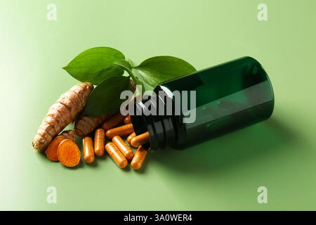Kurkuma Kapseln, Wurzeln und umgedrehte medizinische Flasche auf grünem Hintergrund Stockfoto
