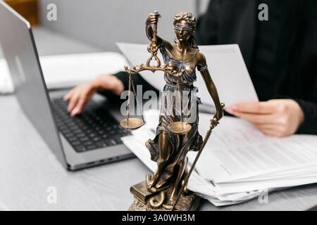 Nahaufnahme eines Anwaltspults mit einem Laptop, einer Brille und einer Statue von Themis. Ein Symbol für Gerechtigkeit und Professionalität im juristischen Bereich. Stockfoto