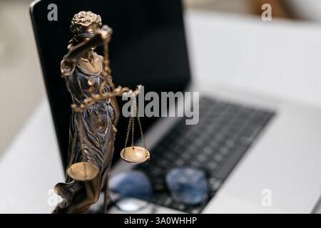 Nahaufnahme eines Anwaltspults mit einem Laptop, einer Brille und einer Statue von Themis. Ein Symbol für Gerechtigkeit und Professionalität im juristischen Bereich. Stockfoto