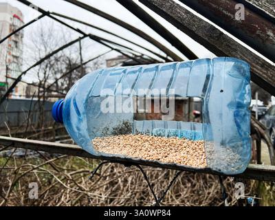Eine selbstgebaute Vogelfuttermaschine, die aus einer Flasche hergestellt wird und Körner enthält, die Vögel finden können. Stockfoto