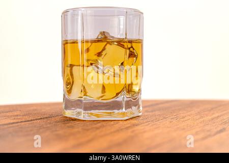Nahaufnahme eines Glases Whiskey auf den Felsen, auf einer hölzernen Oberfläche, mit einem verschwommenen weißen Hintergrund. Stockfoto