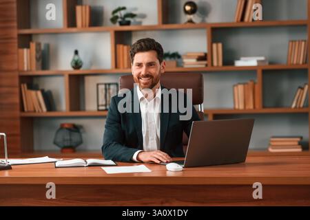 Mit Laptop. Geschäftsmann in formeller Kleidung arbeitet drinnen. Stockfoto