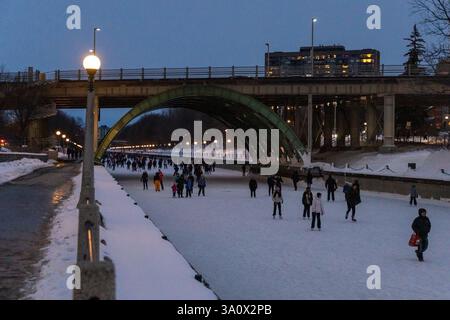 Ottawa, Kanada - 8. Februar 2025: Im Winter läuft man auf dem Rideau Canal unter der Brücke. Am Abend in der Innenstadt Stockfoto