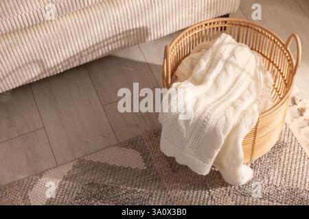 Korb mit gestrickter Decke auf dem Boden drinnen Stockfoto