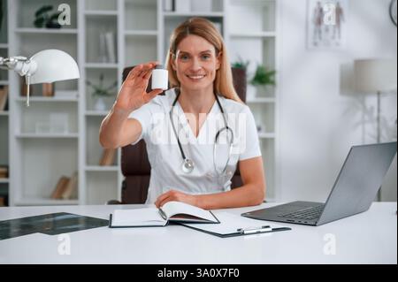 Pillen halten. Die junge Ärztin im weißen Mantel ist drinnen. Stockfoto