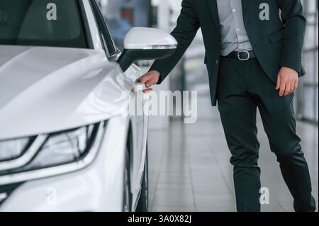 Nahaufnahme eines Mannes im Anzug, der die Tür des neuen weißen Autos öffnet. Stockfoto