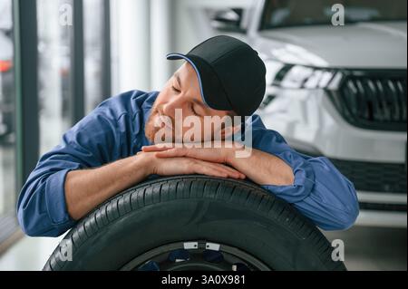 Neuer Reifen. Sich darauf zu stützen. Ein Mann in blauer Uniform arbeitet im Autodienst. Stockfoto