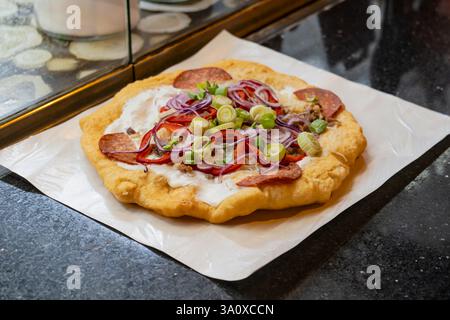 Langos nach ungarischer Art ist ein gebratenes Brot mit Sauerrahm, Käse, Paprika, roten Zwiebeln, Salami und Speck. Stockfoto