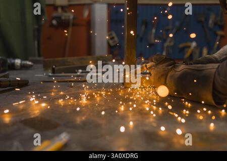 Schweißer in Schutzausrüstung, der mit Metall arbeitet, indem er eine Schweißmaschine verwendet, die helle Funken, Blitze und Dämpfe erzeugt. Stockfoto