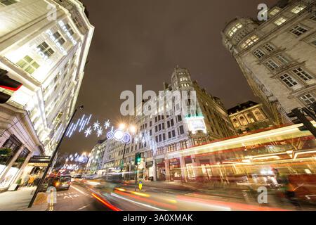 Nächtlicher Blick auf Strand, London. Weihnachtslichter zieren das Strand Palace Hotel und das Savoy Theatre. Viel Verkehr auf der Straße. Stockfoto