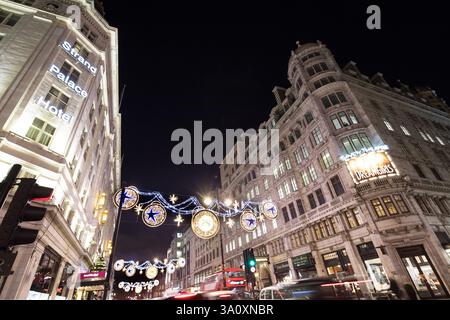 Weihnachtslichter zieren Strand, London, und beleuchten das Strand Palace Hotel und das Savoy Theatre. Nachts ist eine geschäftige Straßenszene zu sehen. Stockfoto