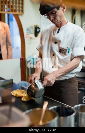 Küchenchef Masanobu Nishikura kocht am 20. Juli 2017 Okonomiyaki-Pfannkuchen auf der Grillplatte im Hauptgeschäft von Boteju in Osaka, Japan. ROB GILHOOLY FOTO Stockfoto