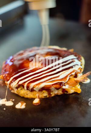 Küchenchef Masanobu Nishikura gießt am 20. Juli 2017 im Hauptgeschäft von Boteju in Osaka, Japan, Mayonnaise auf einen heißen Okonomiyaki-Pfannkuchen. ROB GILHOOLY PH Stockfoto