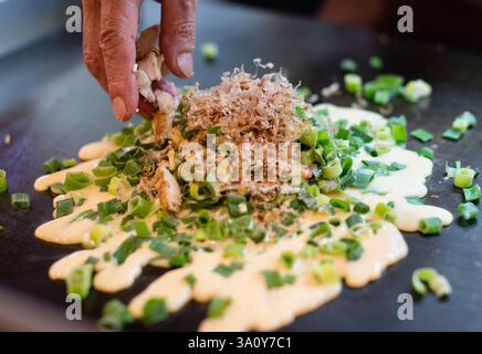 Küchenchef Masanobu Nishikura bestreut am 20. Juli im Hauptgeschäft von Boteju in Osaka, Japan, einen heißen Negi-Yaki-Okonomiyaki-Pfannkuchen Stockfoto