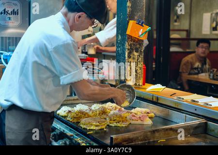 Küchenchef Masanobu Nishikura löffelt den Teig auf die Grillplatte, während er am 20. Juli im Hauptgeschäft von Boteju in Osaka, Japan, Okonomiyaki-Pfannkuchen zubereitet Stockfoto