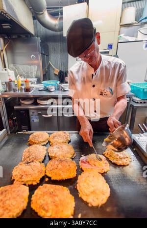 Küchenchef Masanobu Nishikura löffelt den Teig auf die Grillplatte, während er am 20. Juli im Hauptgeschäft von Boteju in Osaka, Japan, Okonomiyaki-Pfannkuchen zubereitet Stockfoto