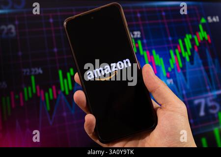 BOGOTA, KOLUMBIEN - 05. MÄRZ 2025 Hand mit einem Smartphone mit Amazon-Logo und verschwommenem Börsenkonzept im Hintergrund Stockfoto