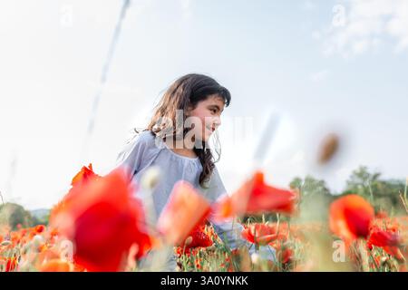 Tiefwinkelansicht eines Mädchens mit langen Haaren, das auf einem Mohnfeld steht Stockfoto