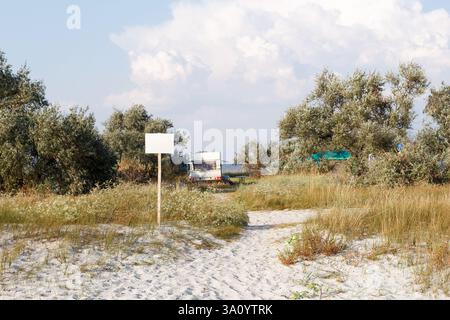Ein Wohnwagen parkt in der Nähe eines Sandstrandes, umgeben von wilder Vegetation und Bäumen, was einen ruhigen und abgeschiedenen Campingplatz schafft. Stockfoto