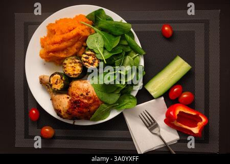 Leckere gebratene Hähnchenkeule mit gerösteter Zucchini, frischen Spinatblättern und einer reichhaltigen, orangenfarbenen Kartoffelpüree- und Kürbismischung. Stockfoto
