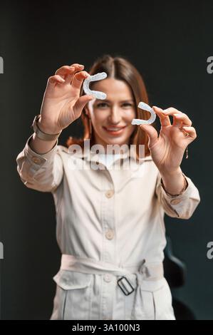 Halten von zwei Ausrichtern. Die junge Frau steht vor schwarzem Hintergrund und hält fest. Stockfoto